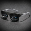 A pair of black polarized sunglasses with a silver strap resting on a dark, speckled surface.