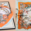 An orange silk scarf with a floral print is displayed on a black tray.