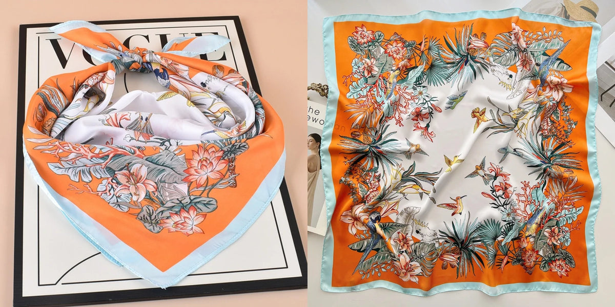 An orange silk scarf with a floral print is displayed on a black tray.