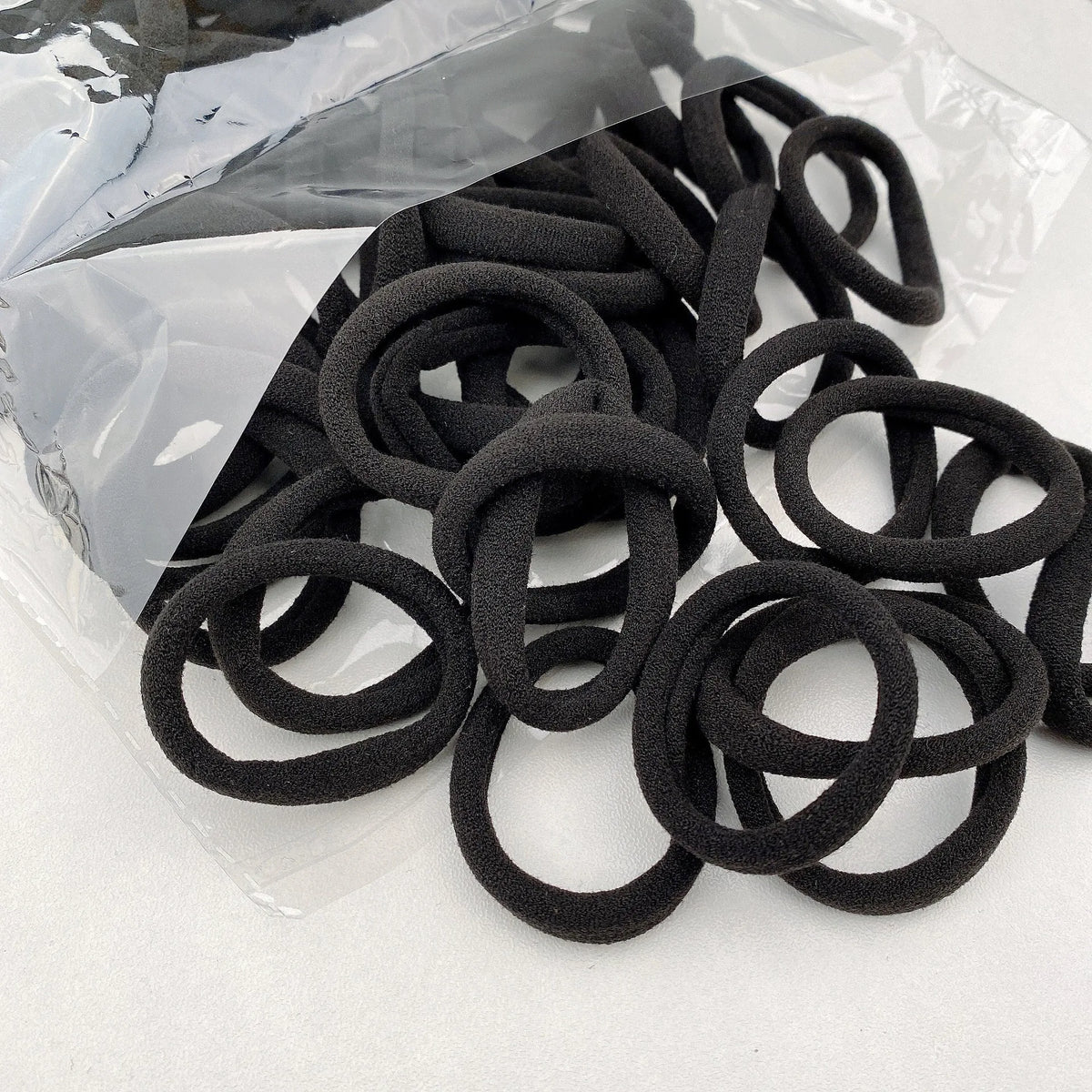 A pile of black elastic hair bands is shown in a clear plastic bag.