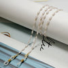 Cordones para gafas de perlas y cuentas elegantes colgados sobre un fondo de papel blanco.