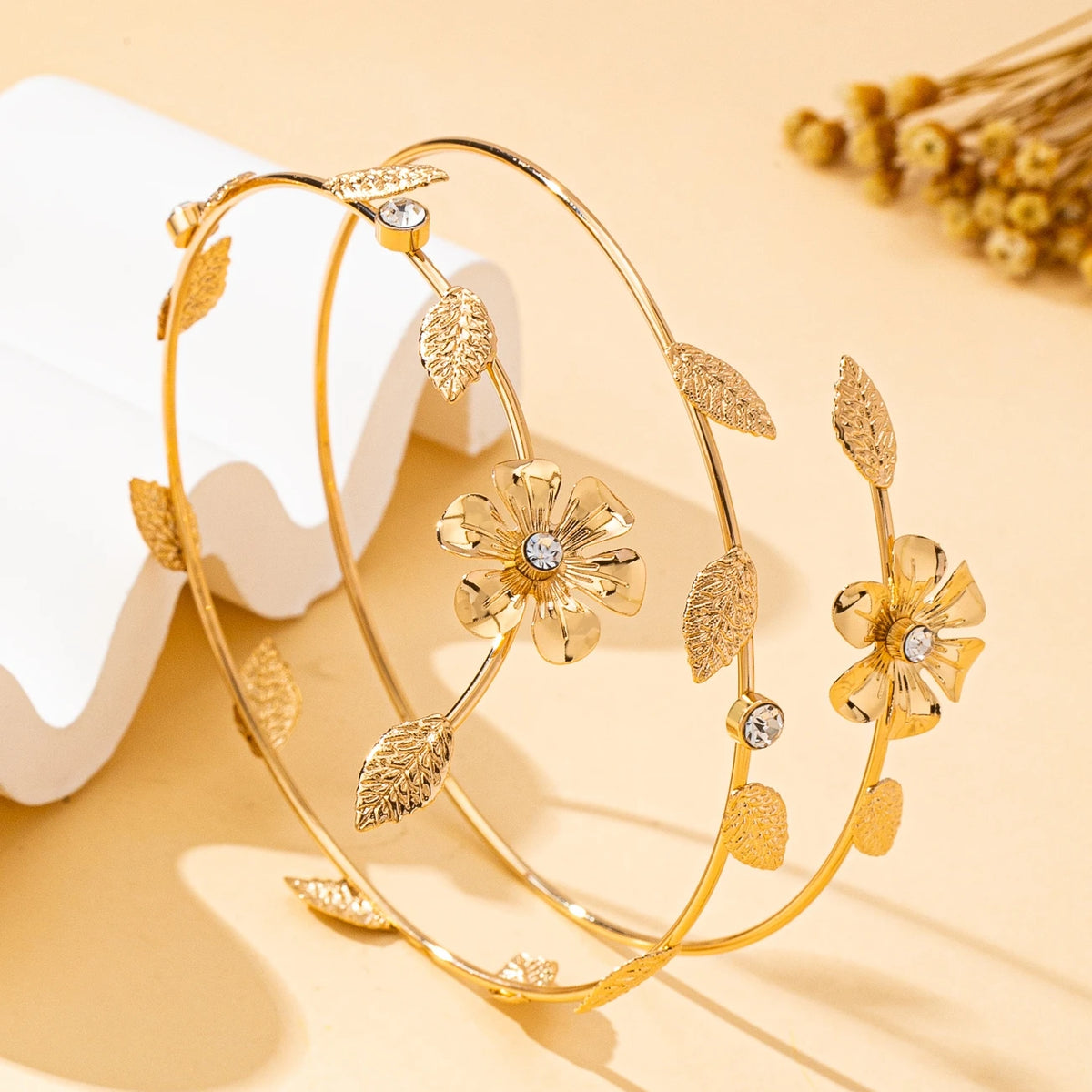 A delicate gold floral vine arm bracelet with small leaves and sparkling accents, displayed on a light background.