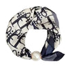 A black and white patterned silk scarf tied in a knot with a pearl magnetic clasp.