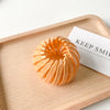 A close-up of an elegant orange horsetail hair clip resting on a wooden tray next to a card.