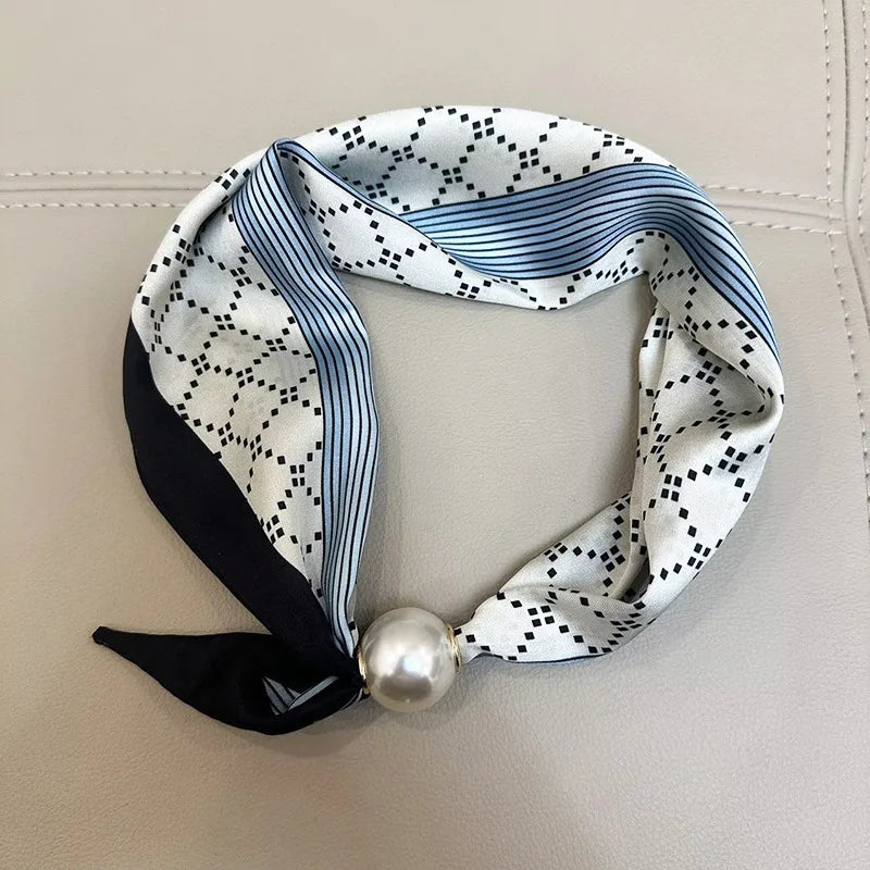 A silk scarf featuring a white background with black polka dots and blue stripes, tied with a pearl magnetic clasp.