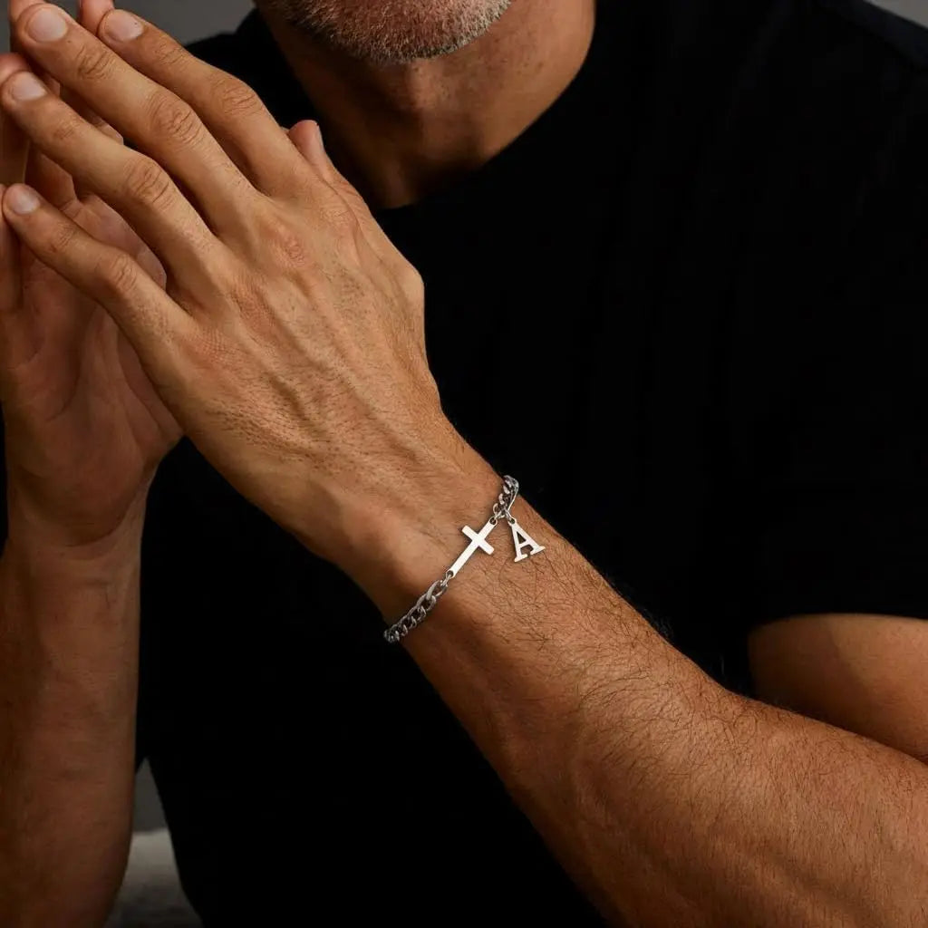A close-up of a man's wrist wearing a silver stainless steel cross Cuban chain bracelet.