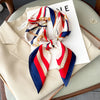 A luxury silk scarf featuring red, white, and blue stripes tied in a bow, displayed on a white card.