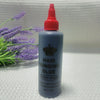 A bottle of professional hair bonding glue with a red cap and dark blue body sits on a light surface next to purple lavender 