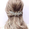 A woman's light blonde hair is styled in a low ponytail with an elegant silver leafed crystal hair comb.