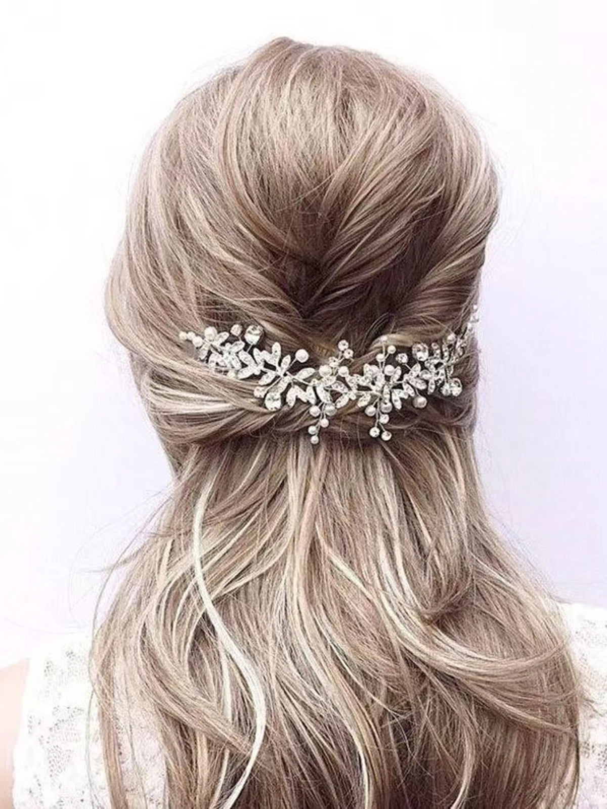 A woman's light blonde hair is styled in a low ponytail with an elegant silver leafed crystal hair comb.