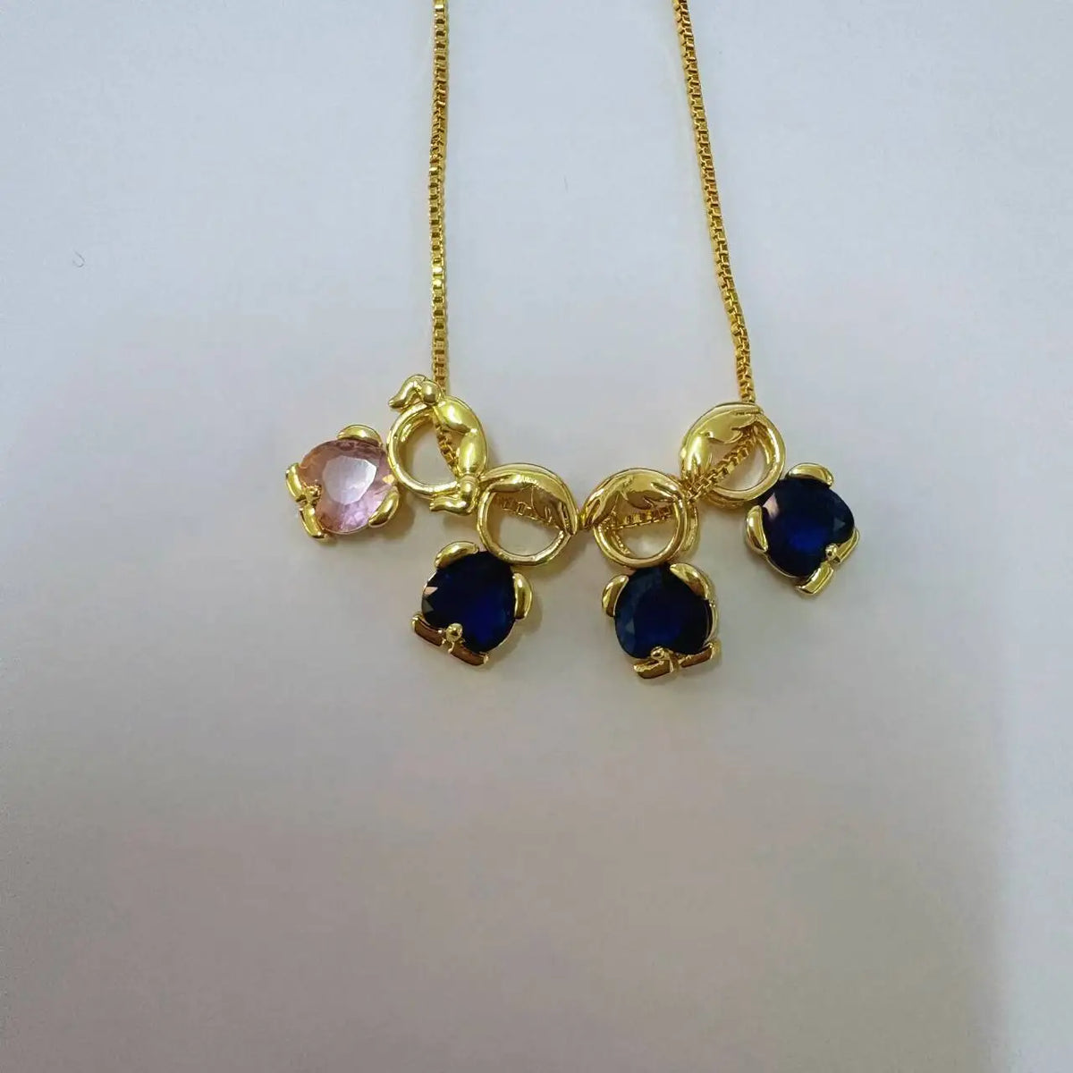 Goldener Anhänger mit pinken und blauen Edelsteinen auf einer goldenen Kette