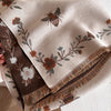 A beige pashmina shawl with a floral print featuring brown and green leaves and small insects.