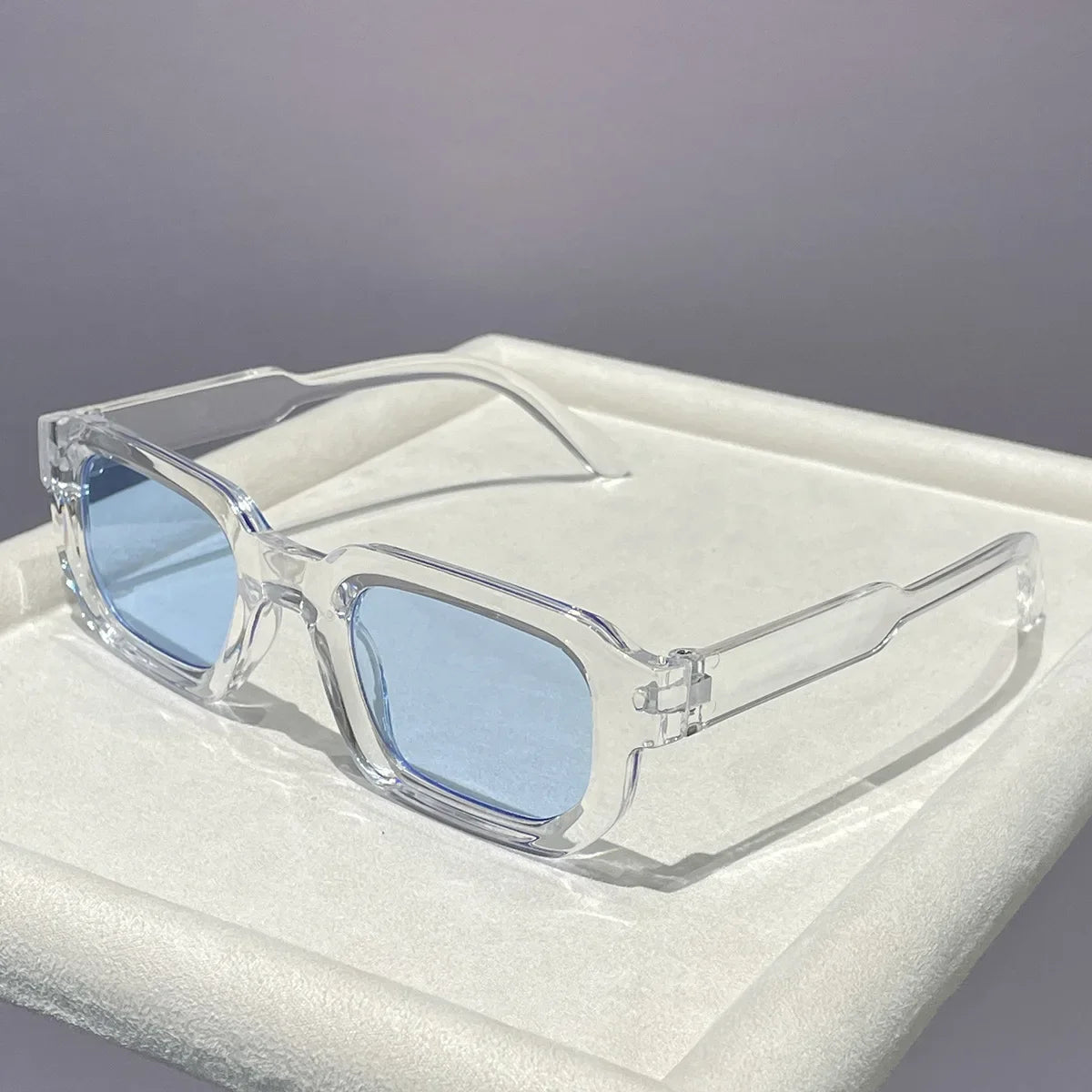 Clear plastic retro square sunglasses with blue lenses resting in a white box.