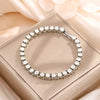 A silver rhinestone stacking bracelet set is displayed on a light pink box with soft fabric in the background.