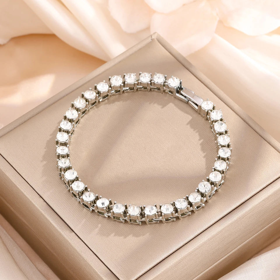 A silver rhinestone stacking bracelet set is displayed on a light pink box with soft fabric in the background.