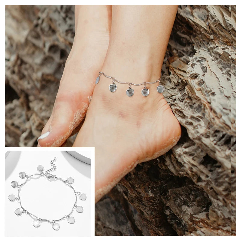 Stainless steel snake chain anklet worn on the ankle against a textured rock surface.