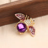 Broche ton or avec motif d'abeille et accents émail rose et violet sur une surface en bois.