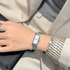 A close-up of a woman's wrist wearing a vintage gold stainless steel quartz watch and a striped cuff, set against a light bla