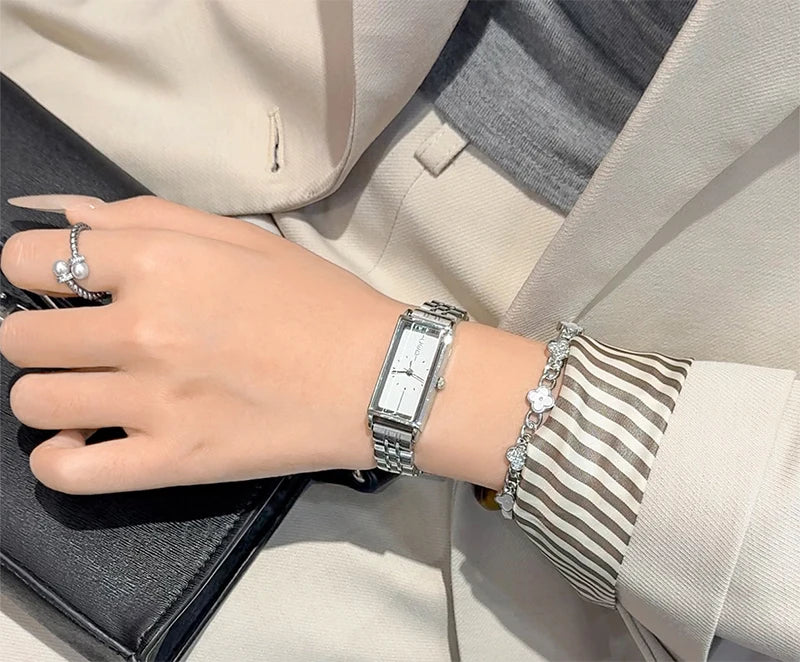 A close-up of a woman's wrist wearing a vintage gold stainless steel quartz watch and a striped cuff, set against a light bla