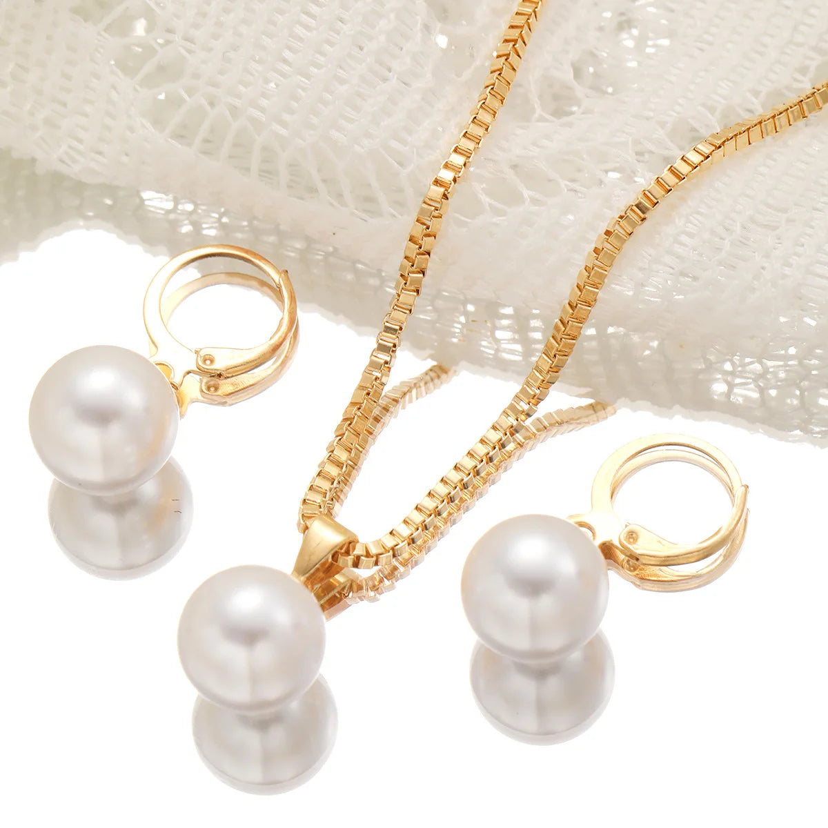 A set of dainty gold pearl jewelry featuring matching earrings and a delicate chain necklace displayed on a white lace fabric