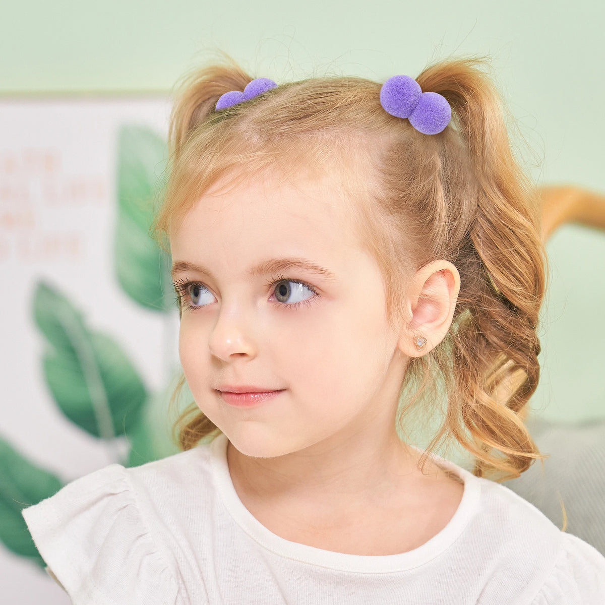 A young girl with blonde hair is shown wearing purple plush elastic hair bands.