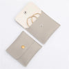 A light beige PU leather jewelry pouch with a snap button closure and a gold-toned strap.
