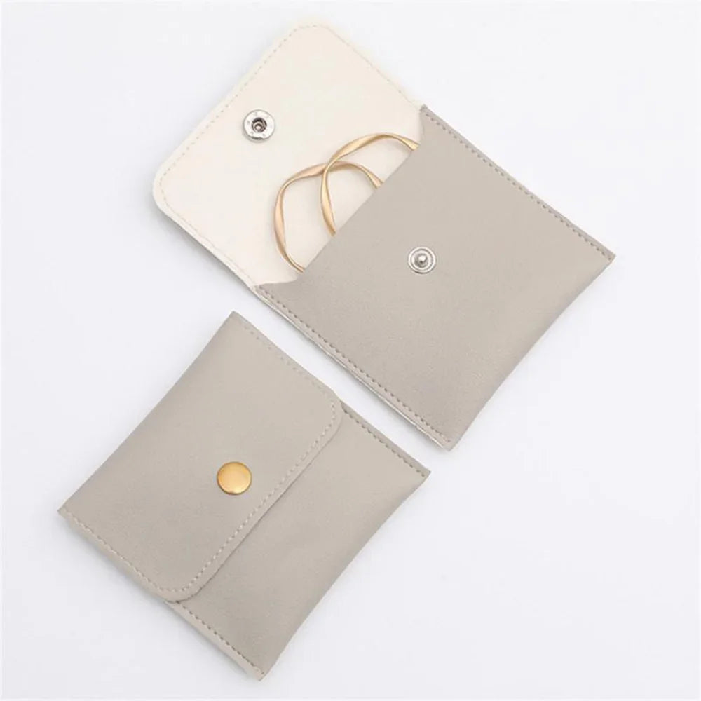 A light beige PU leather jewelry pouch with a snap button closure and a gold-toned strap.