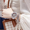 A close-up of a woman wearing a silver watch and holding a brown leather handbag.