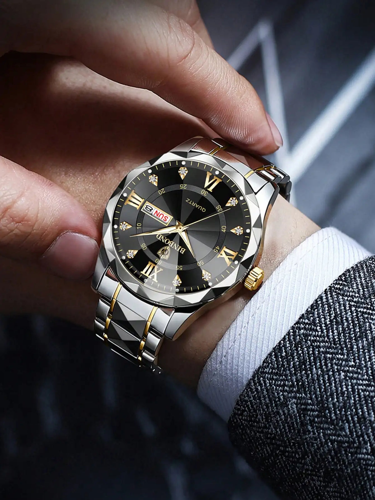 A close-up shot of a stainless steel watch being held on a wrist, featuring a black dial and gold accents.