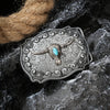 Boucle de ceinture en métal argenté avec une tête d'agneau détaillée et incrustation turquoise, posée sur une pierre sombre.
