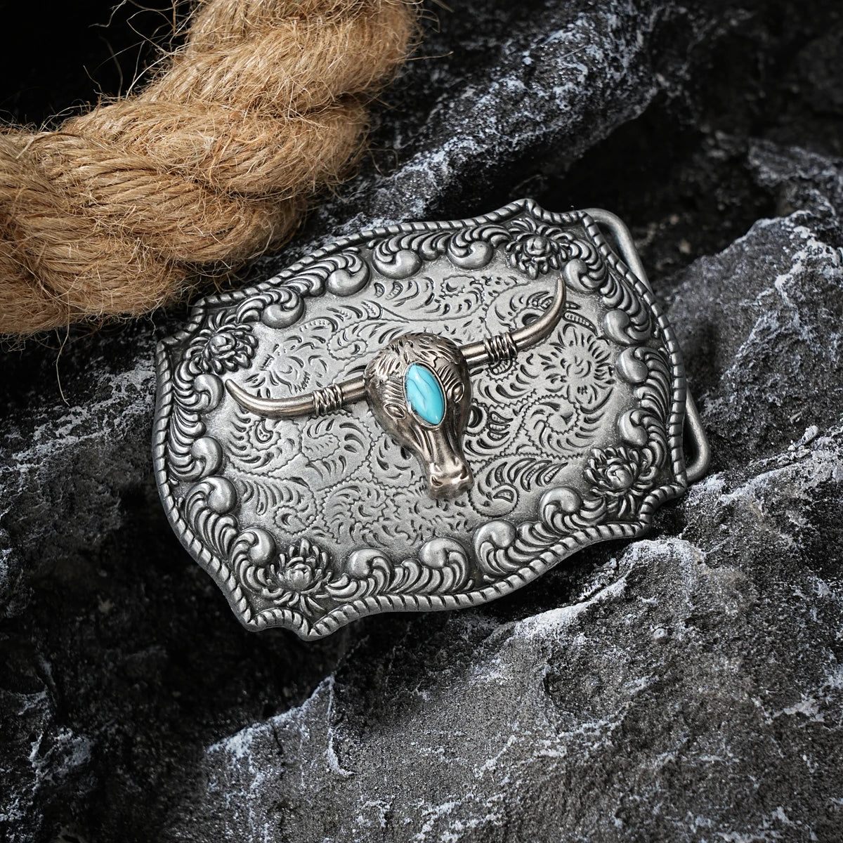 Boucle de ceinture en métal argenté avec une tête d'agneau détaillée et incrustation turquoise, posée sur une pierre sombre.