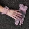 Pink lace tulle finger gloves worn on a hand against a dark gray fabric background.
