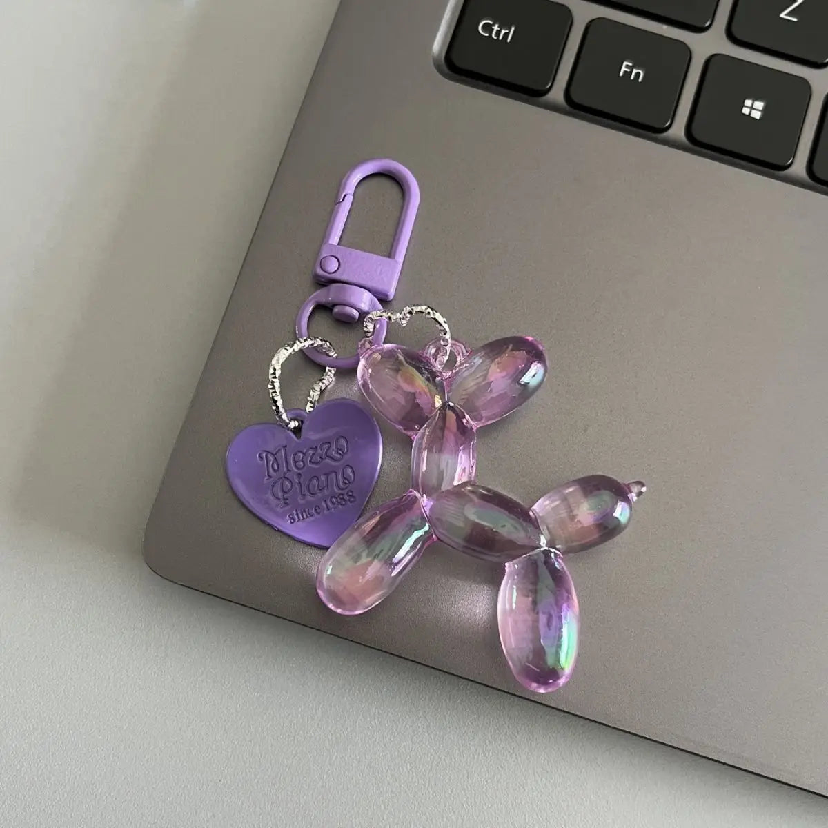 A purple resin animal dog keychain with a silver chain and purple clasp resting on a laptop.