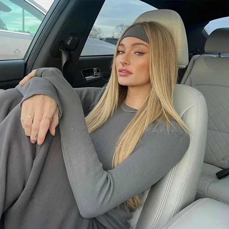 A blonde woman wearing a grey knitted sports headband sits in a car seat.