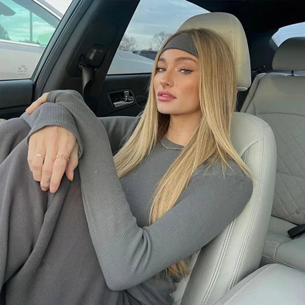 A blonde woman wearing a grey knitted sports headband sits in a car seat.