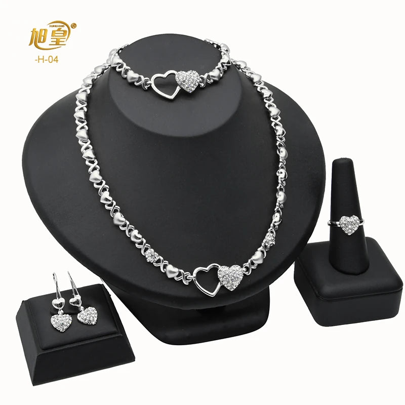 A silver heart crystal necklace and matching earrings displayed on a black stand.