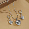 Silver heart necklace and earring set displayed on a beige background
