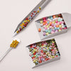 Stainless steel tool with a long needle used to move colorful beads into a tray for jewelry making