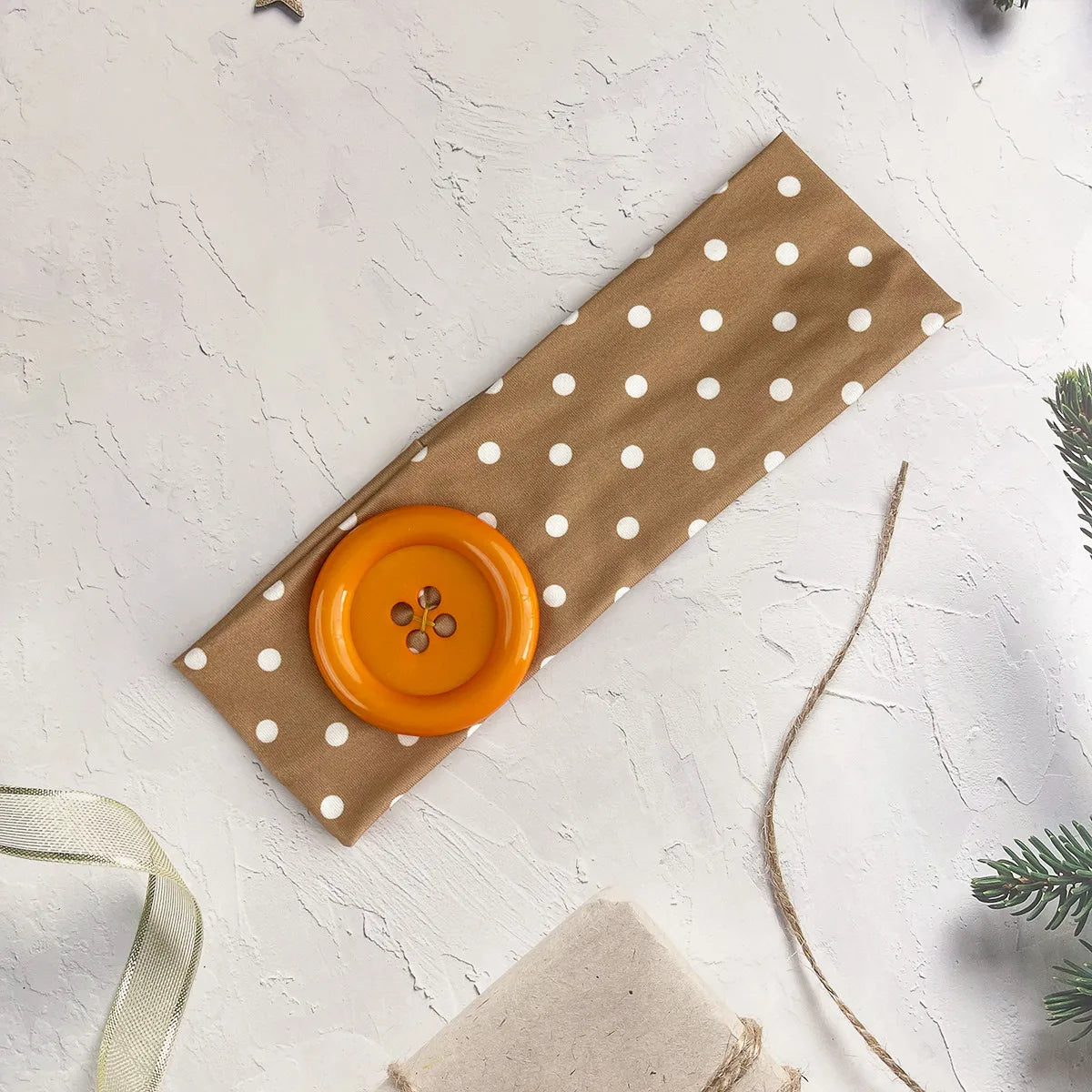 A vintage polka dot button headband in tan fabric with an orange button.