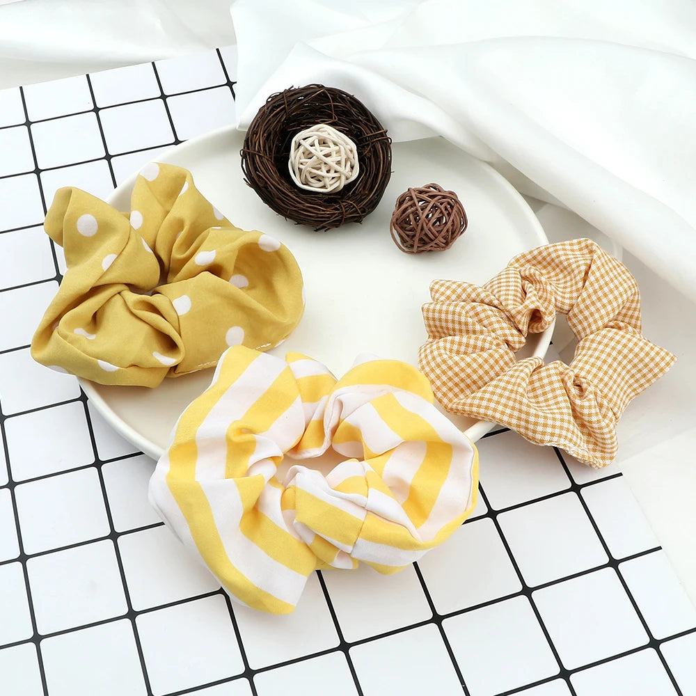 A display of three colorful knitted hair scrunchie headbands in yellow, cream, and plaid patterns on a white plate.