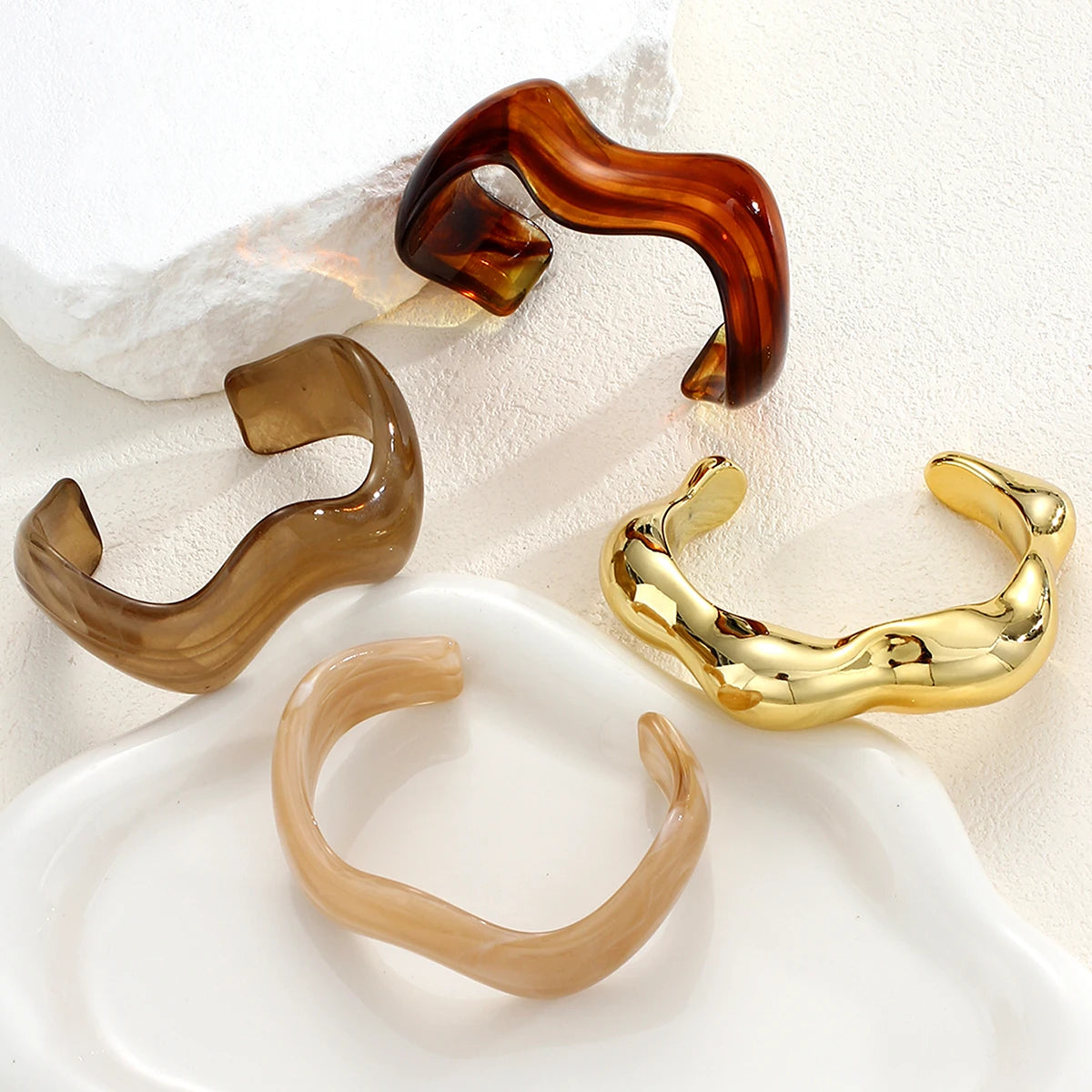 A set of three vintage minimalist wavy bangle bracelets in shades of brown, gold, and beige displayed on a white surface.