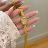 A hand is holding a gold-toned quartz fashion wristwatch with a gold chain and round face against a light background.