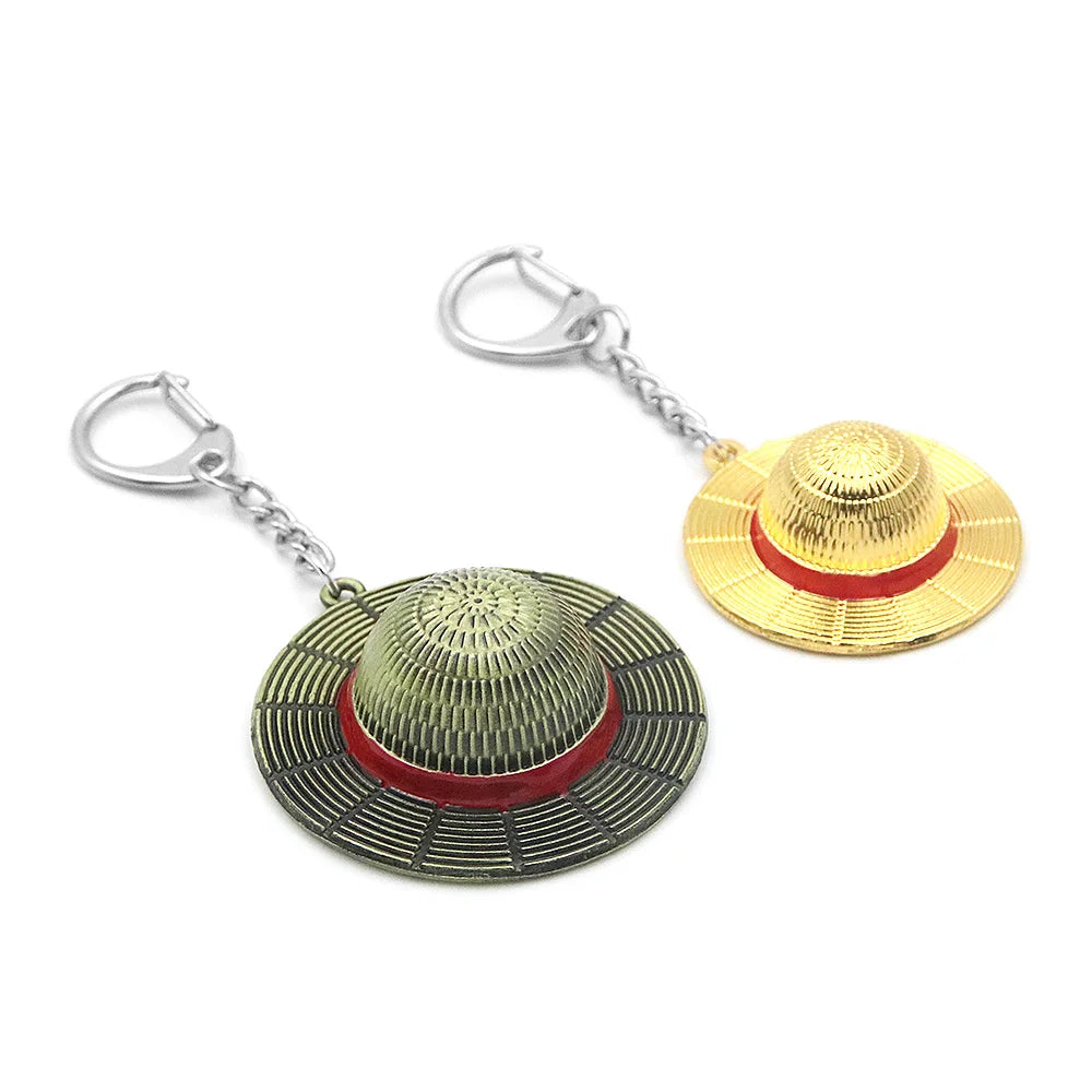 A gold-toned anime style straw hat metal keychain with a red band and silver jump ring.