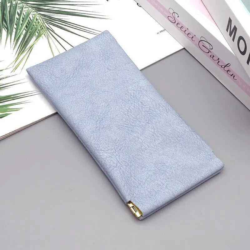 A light blue premium PU leather eyewear storage bag lying on a gray surface next to a book.
