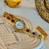 Goldene Modeuhr mit farbigen Edelsteinen und Strass auf beigem Gewebe.