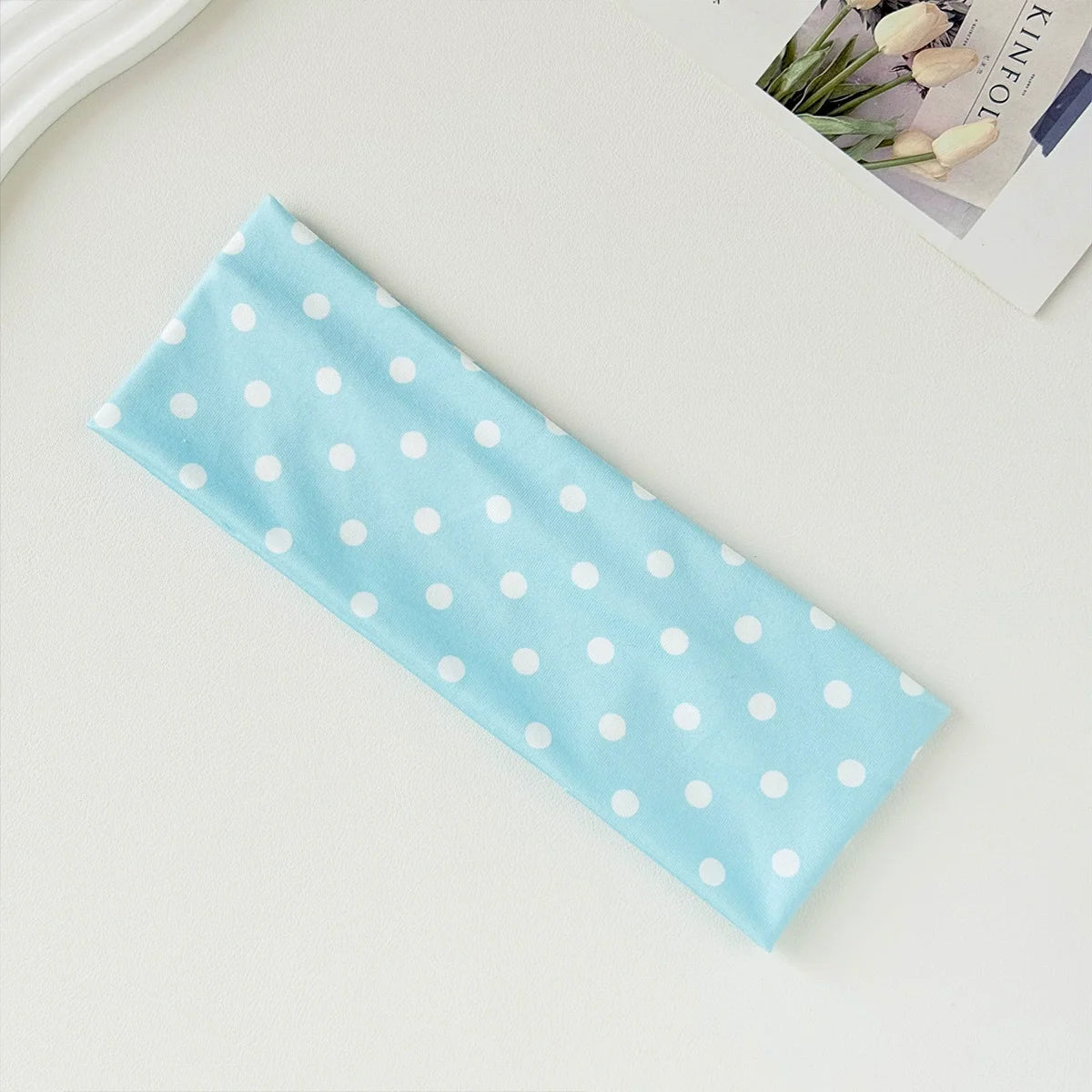 Light blue fabric hairband with white polka dots lying on a light surface.
