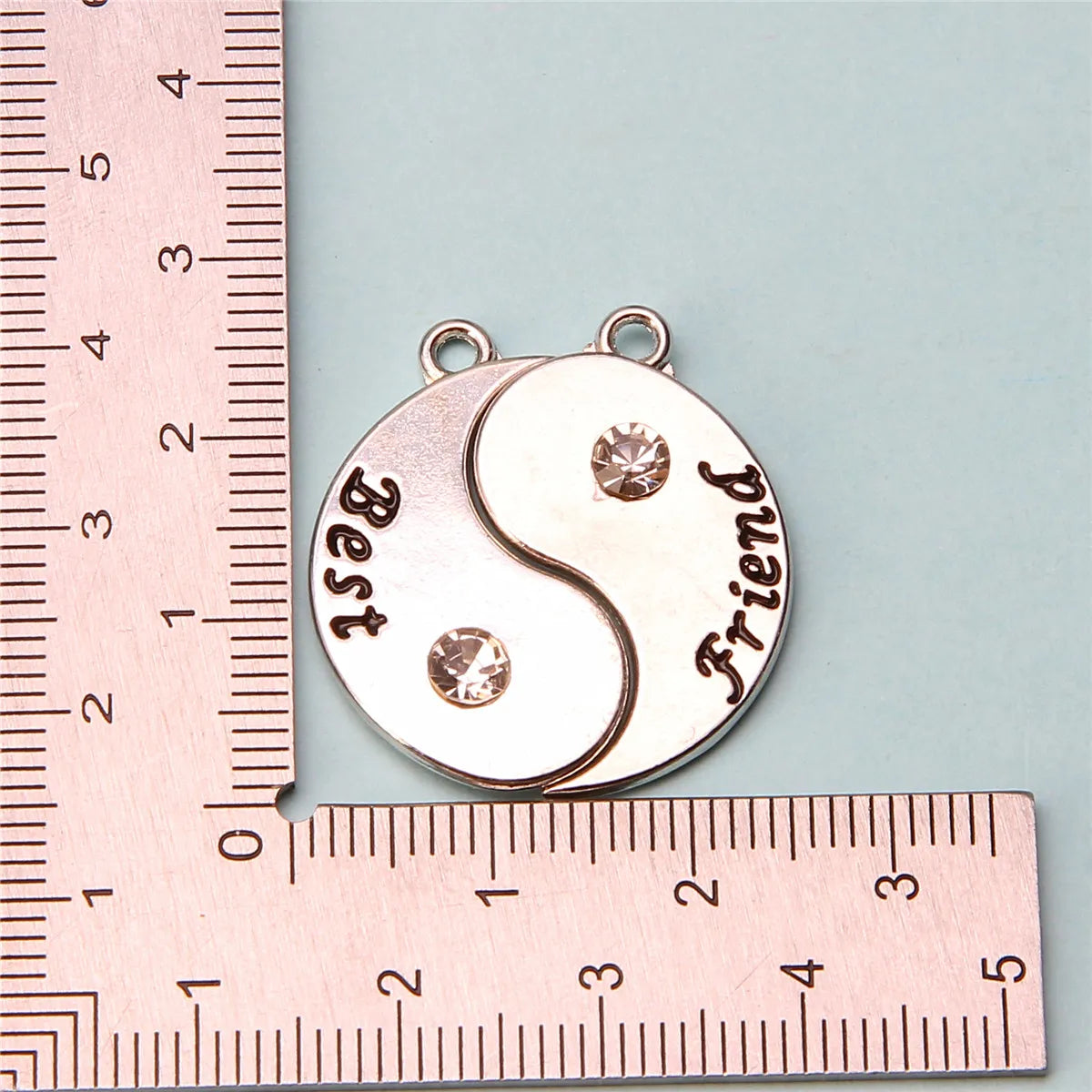 Collar de amistad plateado con dos colgantes estilo yin-yang marcados Best y Friend, medido con una regla.