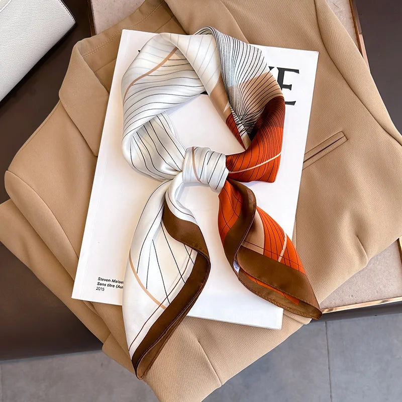 A luxury silk scarf tied in a bow with striped patterns in beige, white, and burnt orange tones, displayed on a tan blazer.