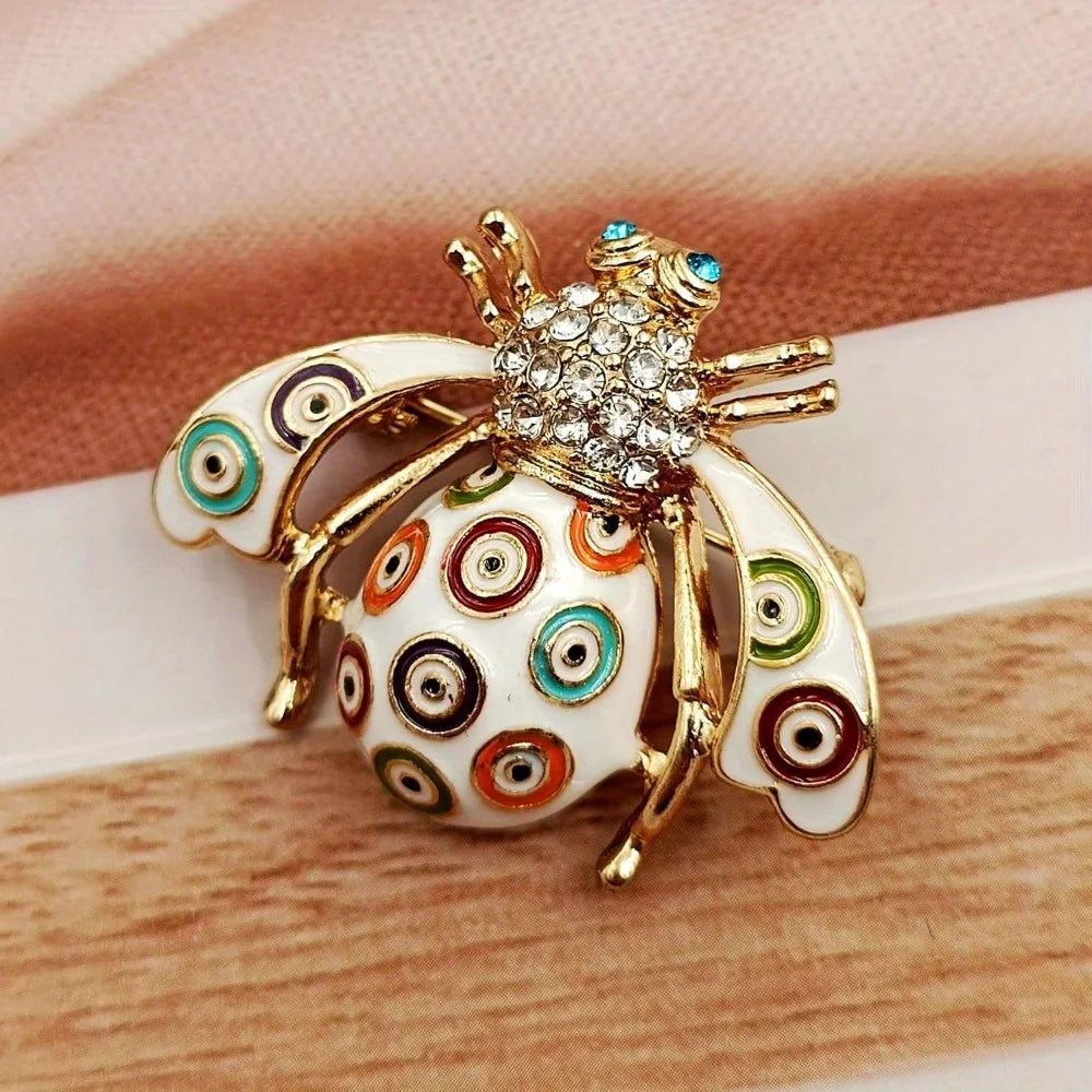 Broche dorée avec motif d'abeille et motifs circulaires iridescents et colorés sur les ailes
