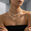 A close-up of a woman wearing a delicate gold and pearl boho shell starfish necklace.